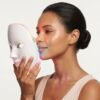 Woman holding LED facial mask in side profile with rainbow light